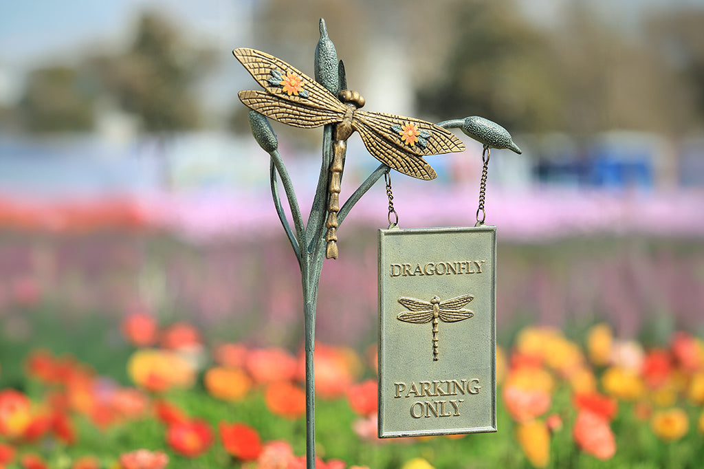 Decorative metal dragonfly sign with 'Dragonfly Parking Only' text in a garden setting.