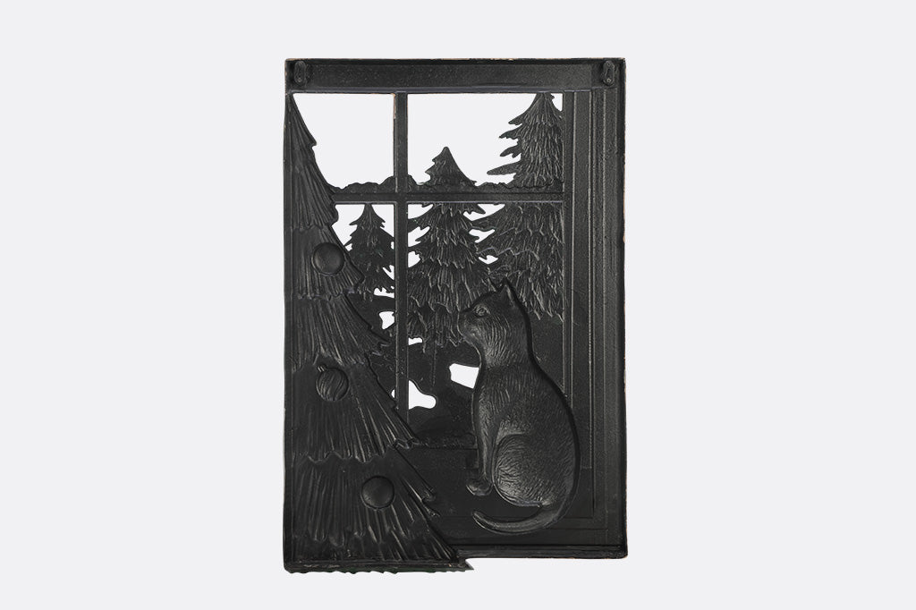 A decorative wall art of a cat looking out a window at trees next to a Chirstmas tree.