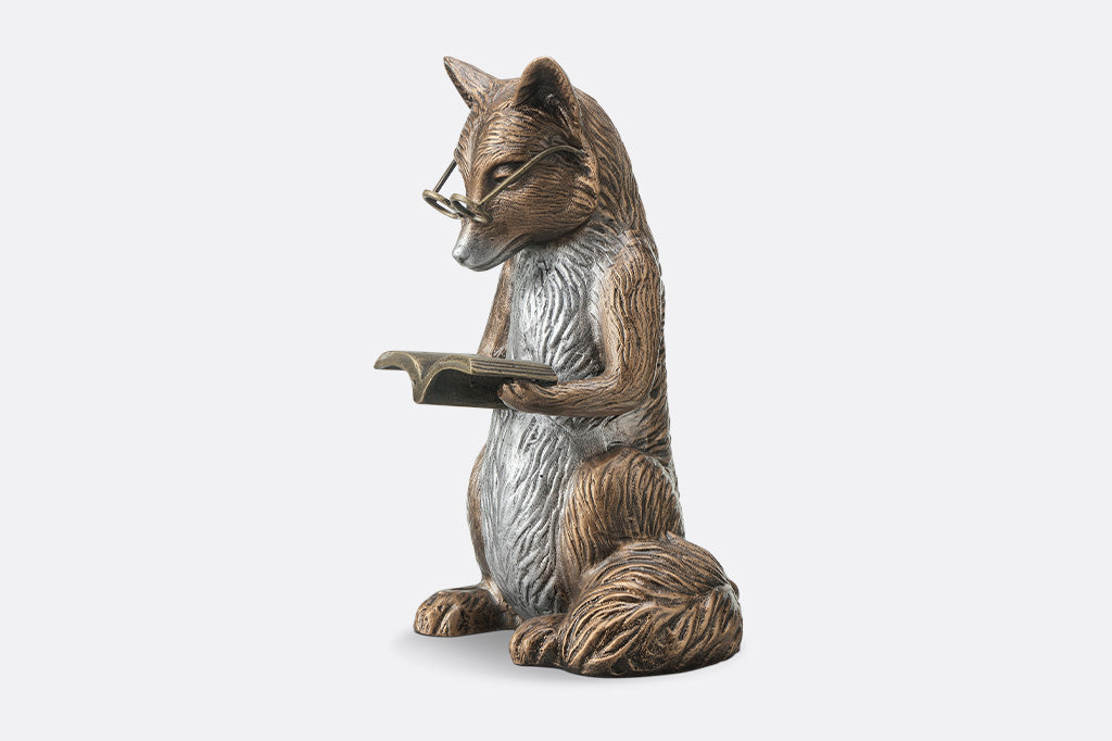 Bronze statue of a fox reading a book on a white background