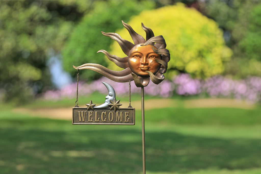 Decorative garden stake with sun and moon design and 'Welcome' sign in a garden setting.