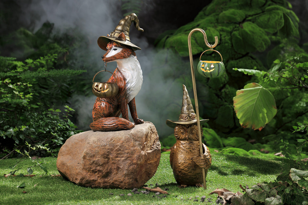 two creatures with witch hats and broomsticks standing on a rock in a forest setting.