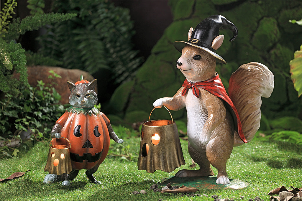 Two animal figurines, one in a pumpkin costume and the other in a top hat and bow tie, standing in a forest setting.