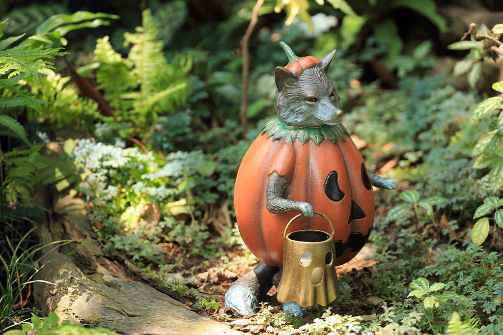 Cat statue in a pumpkin costume with a basket in a garden setting