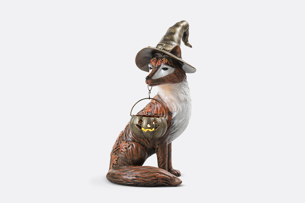 Fox figurine wearing a witch hat with a lantern on a white background