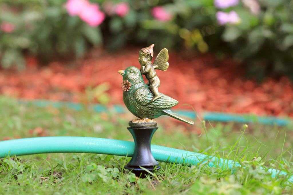 Decorative garden faucet with fairy on a bird design, placed on grass with a hose nearby.