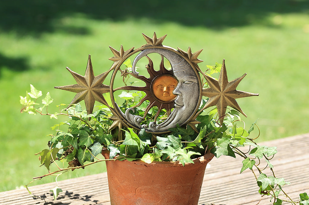 A garden edging with 5 stars, a moon, and a sun placed inside of a potted plant.