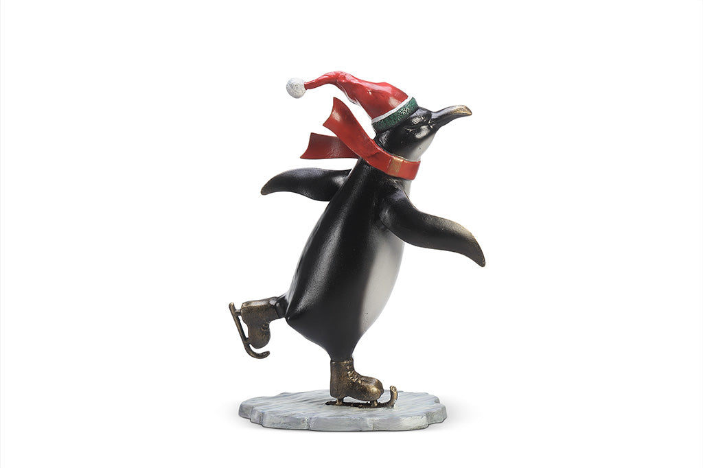 A sculpture of a penguin wearing a scarf and Santa hat ice skating.