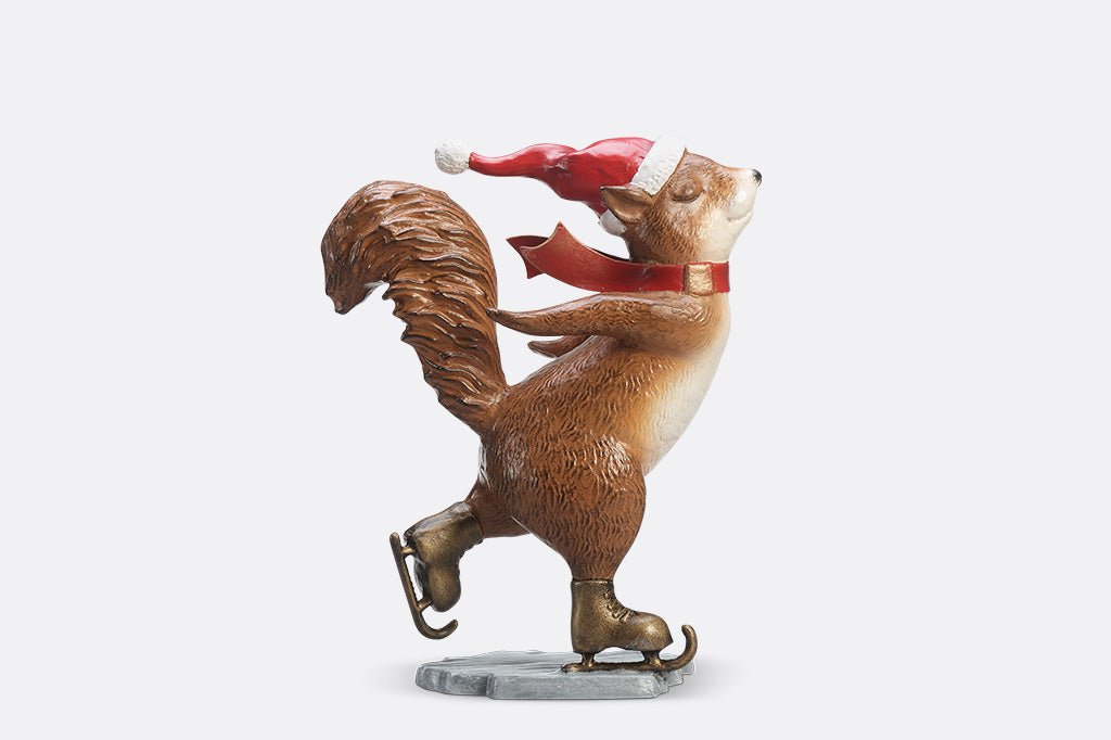 A statue of a squirrel wearing a santa hat and scarf ice skating.