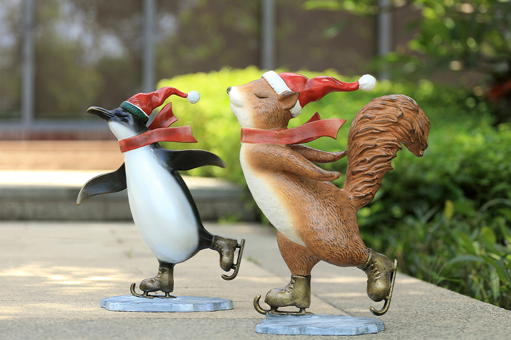 A statue of a squirrel and penguin wearing a santa hat and scarf ice skating.