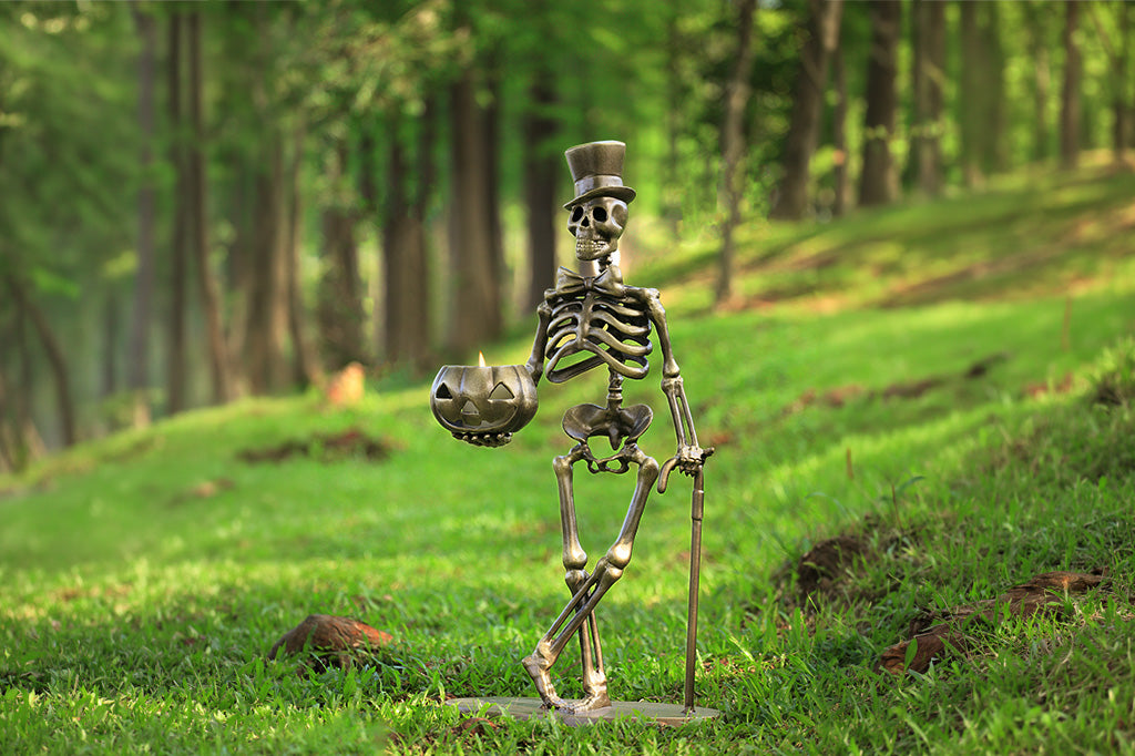 Skeleton figure with a top hat and smoking pipe standing on grass with trees in the background