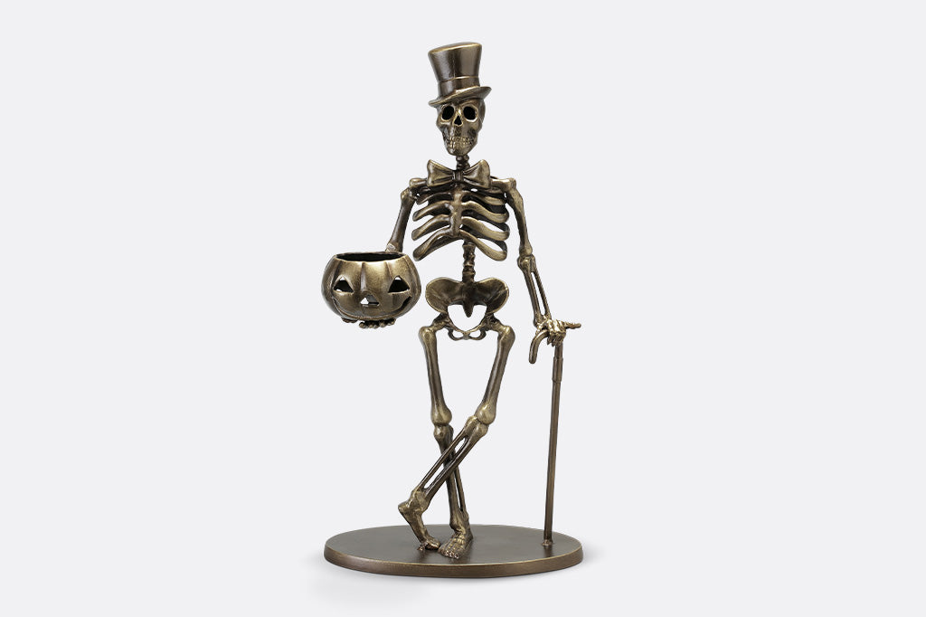 Bronze skeleton figurine with top hat and pumpkin on a white background