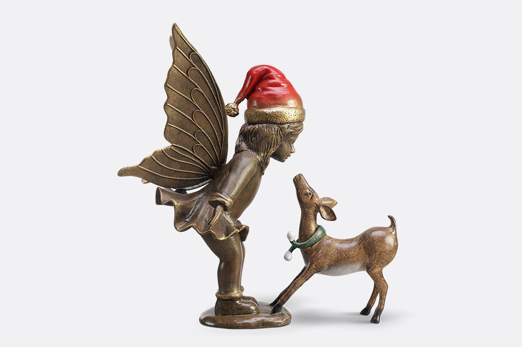 A sculpture of a fairy wearing a santa hat and a deer wearing a scarf playing with each other.