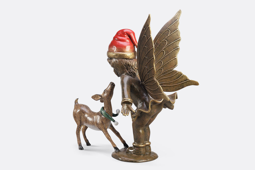 A sculpture of a fairy wearing a santa hat and a deer wearing a scarf playing with each other.