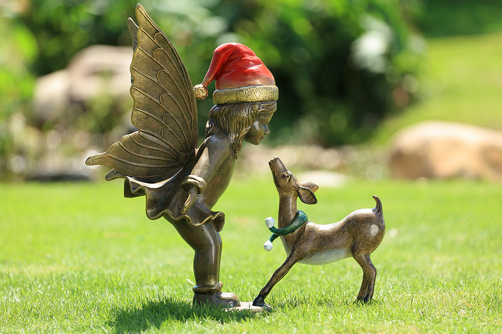 A sculpture of a fairy wearing a santa hat and a deer wearing a scarf playing with each other.
