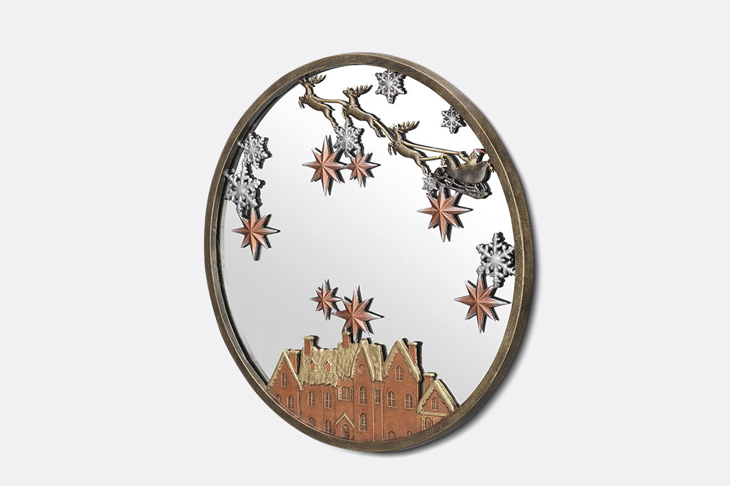 A round mirror with details of Santa and his sleigh being pulled by reindeer across a sky of stars and over rooftops.