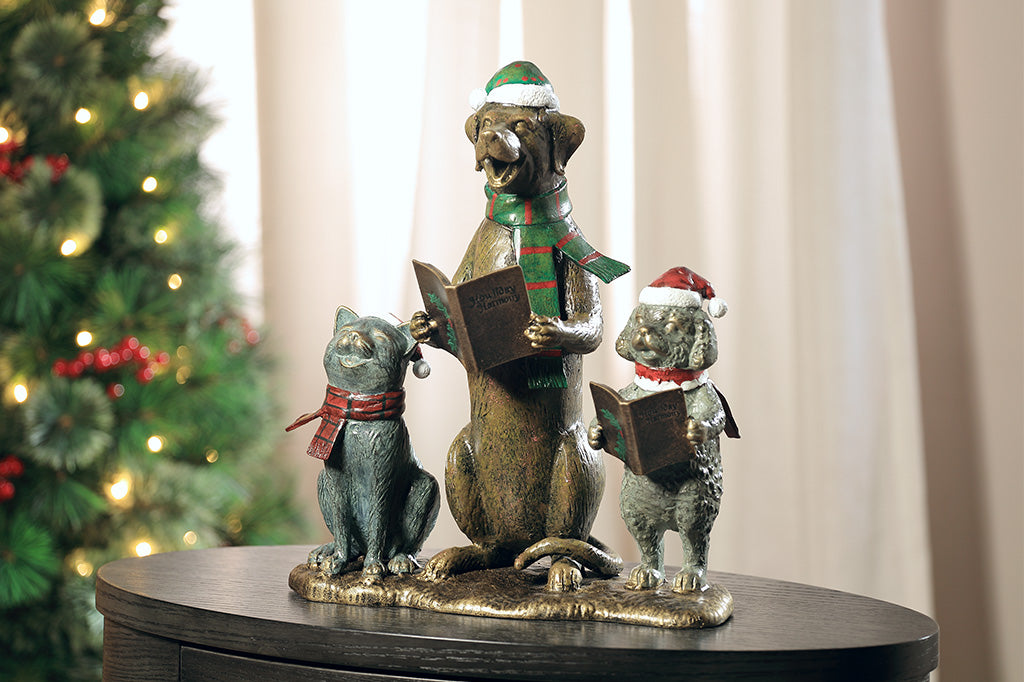A cat and two dogs are singing and dressed in festive christmas attire hold a book of christmas carols.