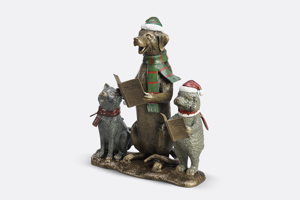A cat and two dogs are singing and dressed in festive christmas attire hold a book of christmas carols.