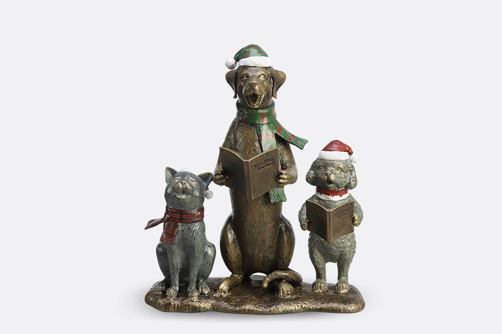 A cat and two dogs are singing and dressed in festive christmas attire hold a book of christmas carols.