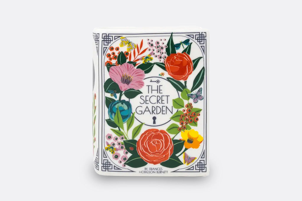 A ceramic and wax candle shaped like a book with flower decorations.