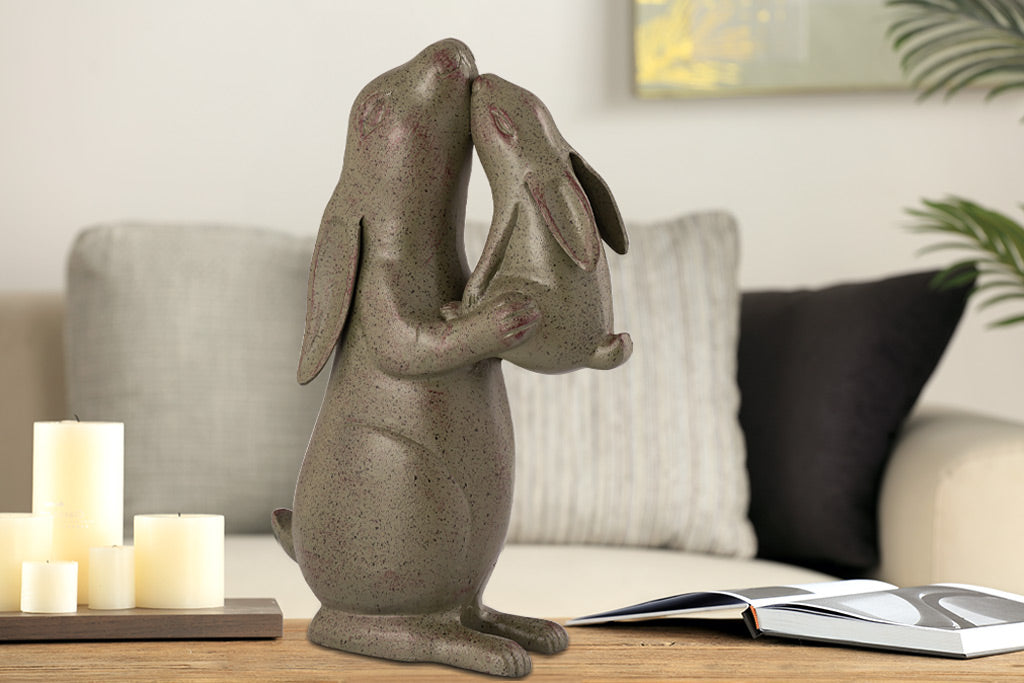 Sculpture of rabbit nuzzling a baby bunny on a coffeetable by a couch in indoor setting