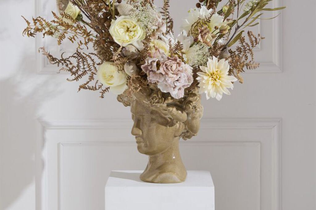 Decorative head sculpture-vase with a floral arrangement against a white wall