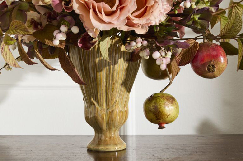 Decorative floral arrangement with pomegranates in a textured vase on a wooden surface.
