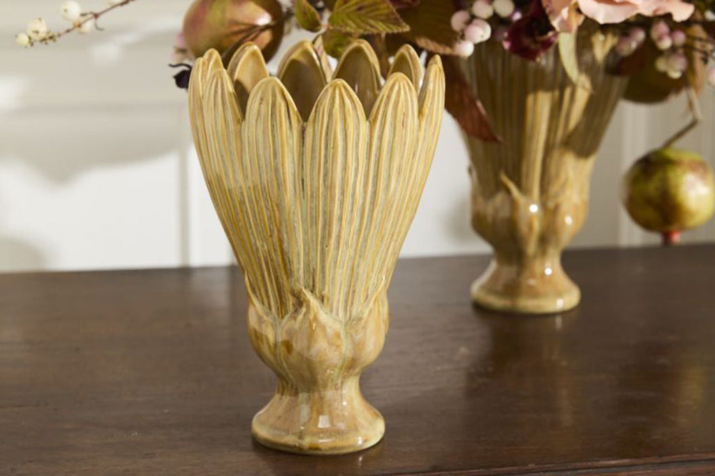 Decorative blossom shaped ochre vase on a wooden surface.