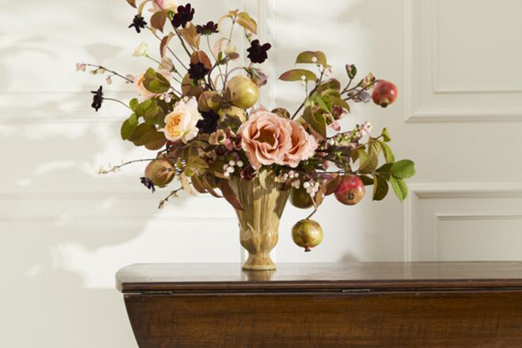 Floral arrangement with pomegranates in a blossom-shaped ceramic vase on a wooden table