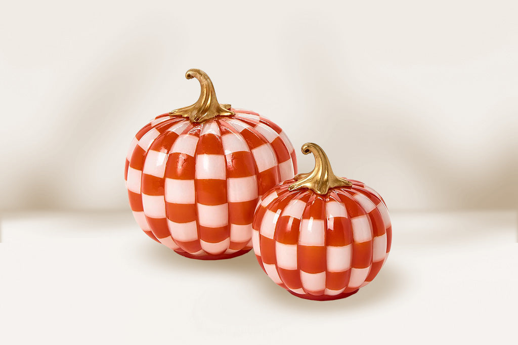 Two orange and white checkered pumpkins with gold stems on a light background