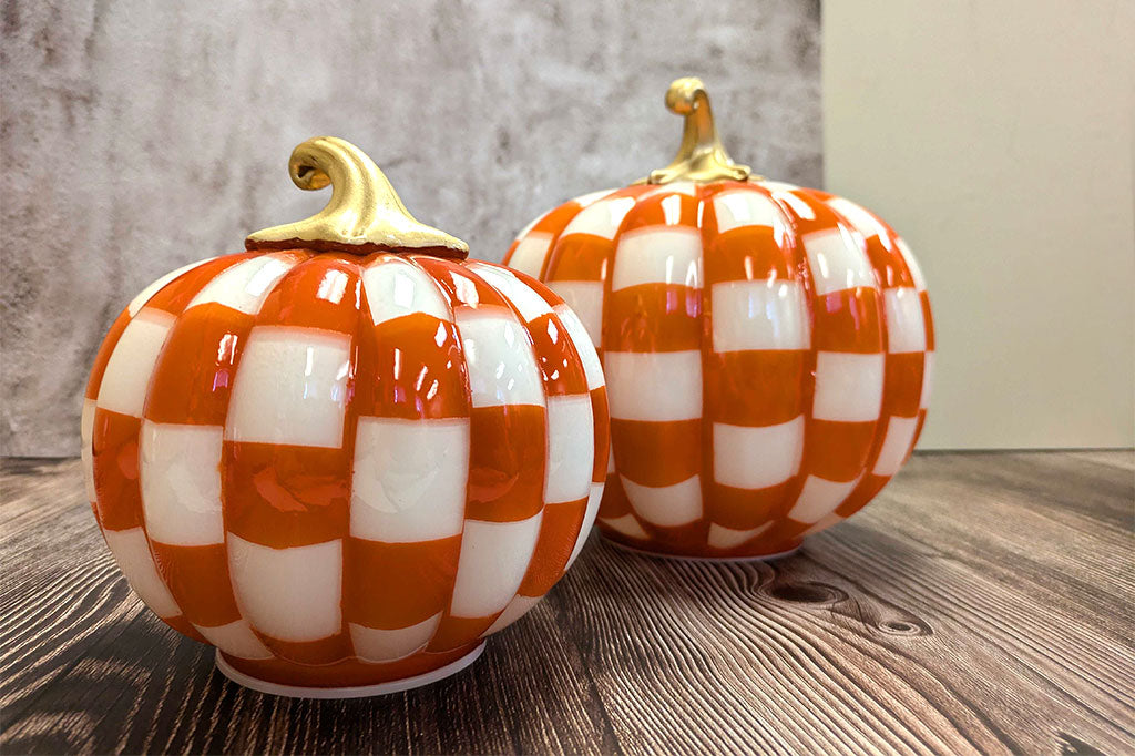 Two decorative pumpkins with orange and white checkered pattern on a wooden surface.