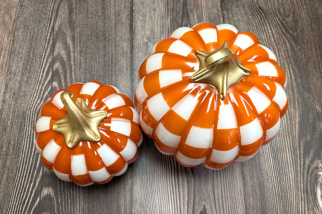 Two decorative pumpkins with orange and white checkered pattern on a wooden surface
