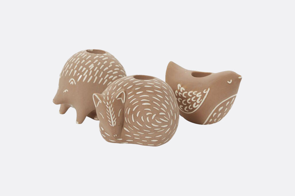 Three ceramic animal-shaped candleholders on a white background. Hedgehog, bird, and fox with white detail accents