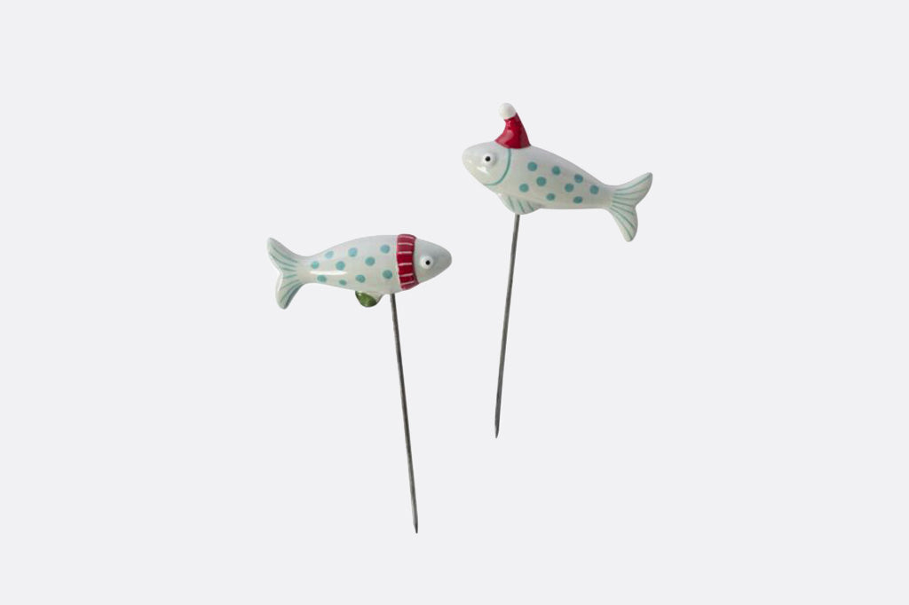 Two small decorative fish picks with metal skewers, featuring white bodies with green polka dots and red holiday accents, shown on a plain light gray background.