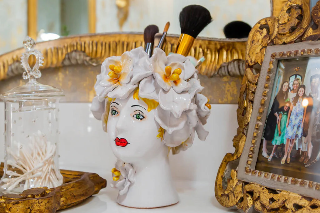 ceramic women's head adorned with big white flowers vase filled with makeup brushes