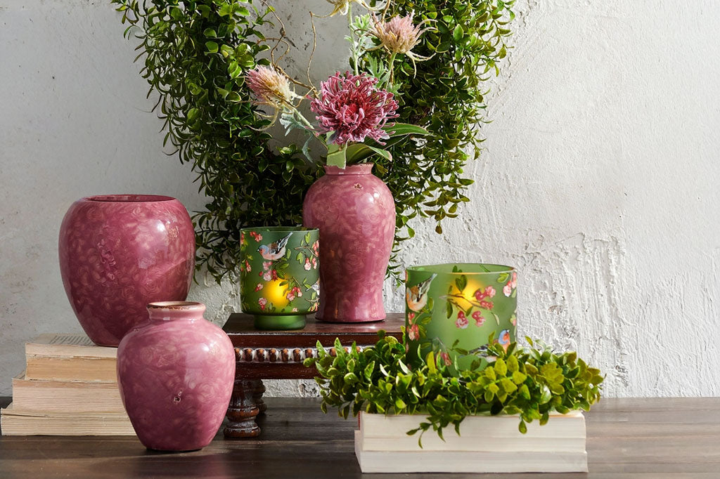 Decorative green glass candleholders shown near to vases, plants and books.