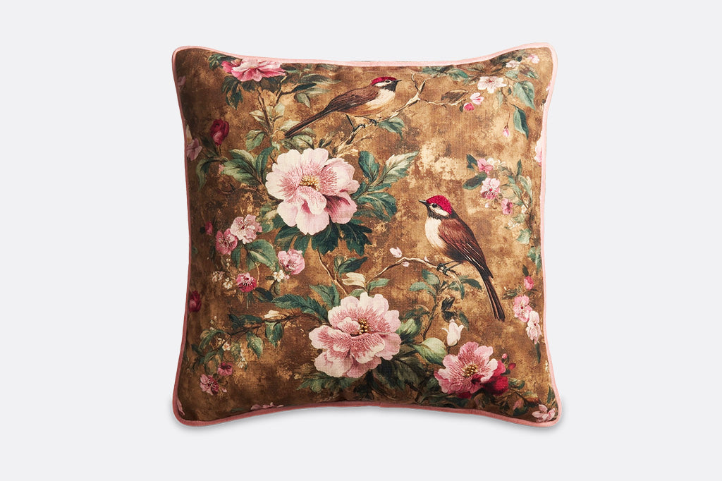 A brown pillow with pink flowers and finches.