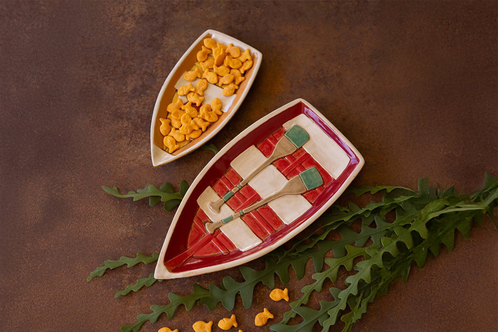 A set of dishes shaped like row boats, one filled with crackers.