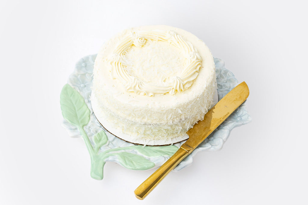 Ceramic serving plate shaped like hydrangea blossom in soft blue with green stem, relief detailing. Shown with decorated cake and gold cake serving knife.