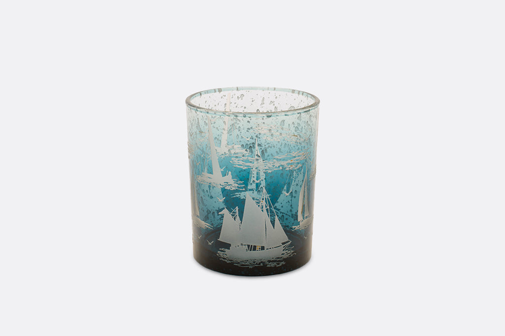 Two candleholders decorated with imagery of sailboats in water.
