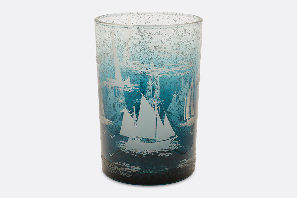 Two candleholders decorated with imagery of sailboats in water.
