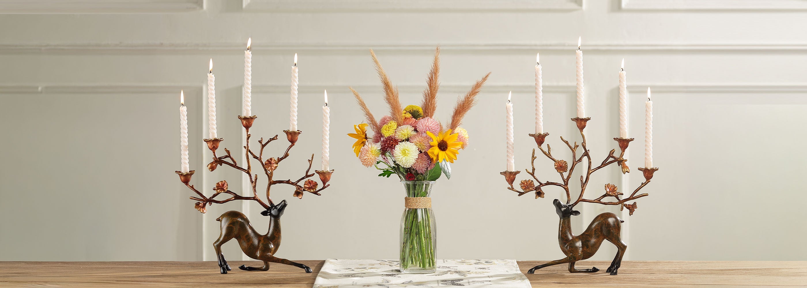 Decorative candle holders shaped like deer with candles and a vase of flowers on a wooden surface.