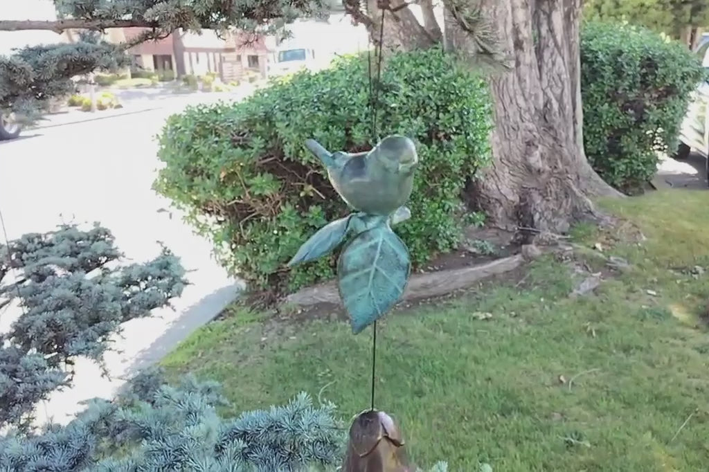 Cast brass bird and blossom shaped bell wind art hanging from tree on a windy day