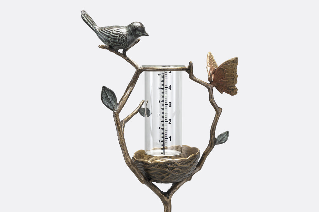 a staked rain catcher in a decorative holder shaped like a nest on a branch, adorned with bird and butterfly