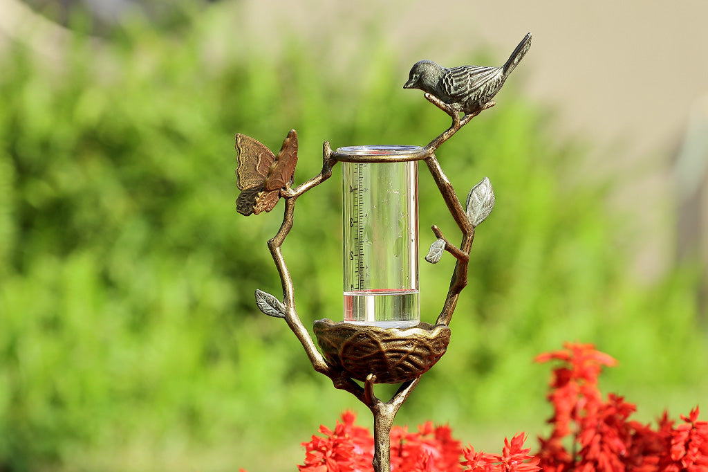 a staked rain catcher in a decorative holder shaped like a nest on a branch, adorned with bird and butterfly