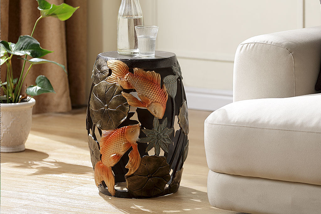 Cast Metal koi fish and water lily garden/ accent stool. golden orange koi surrounded by bronze water lilypad motifs. Shown in room with wood floor, houseplant nearbay, and beige couch.
