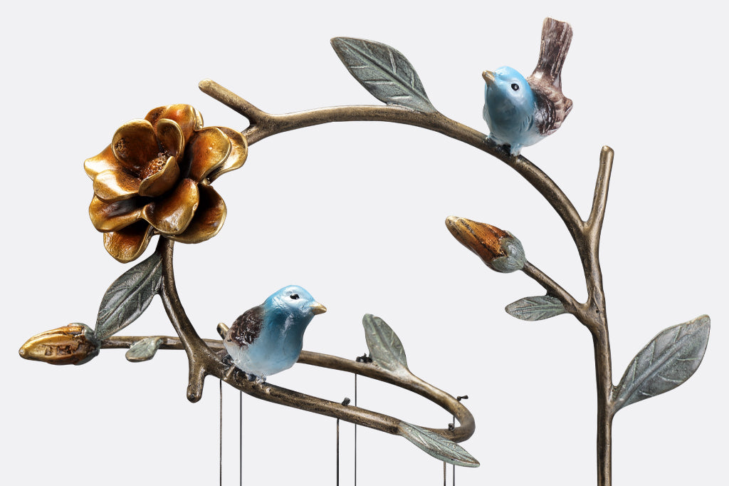 detail view of two cast metal bluebirds perched on branch with leaves and flowers 