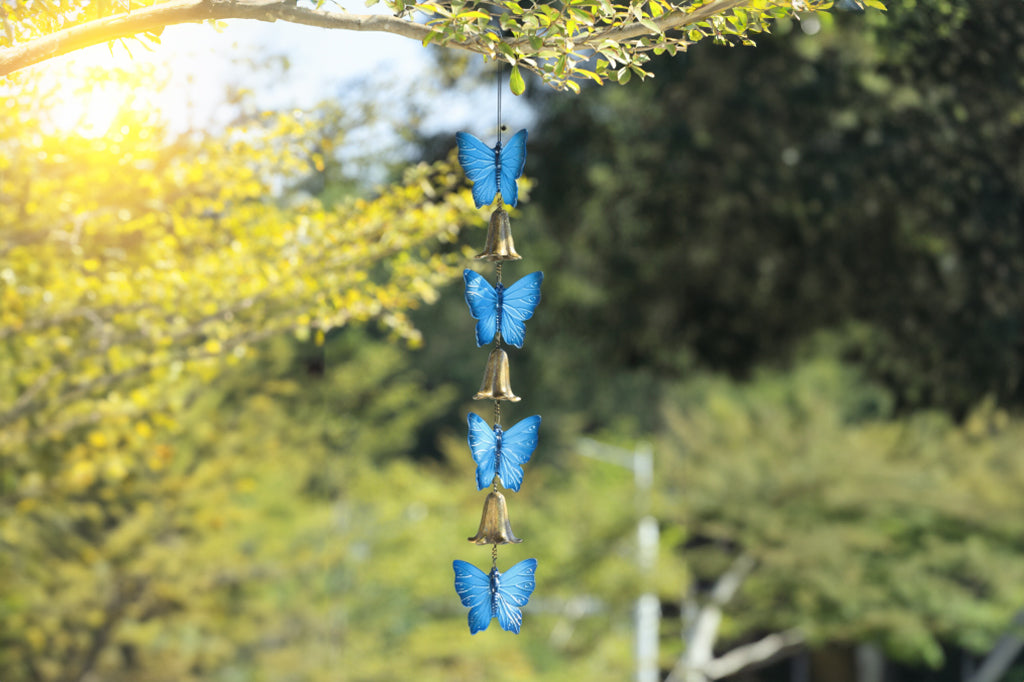 cast metal blue butterfly and bell windchime, hanging from tree in outdoor environment