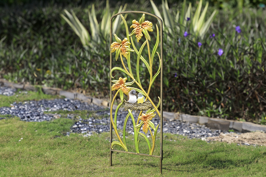 Amongst The Lilies Garden Trellis in a garden. features shimmery pastel finish and a nest with 2 birds