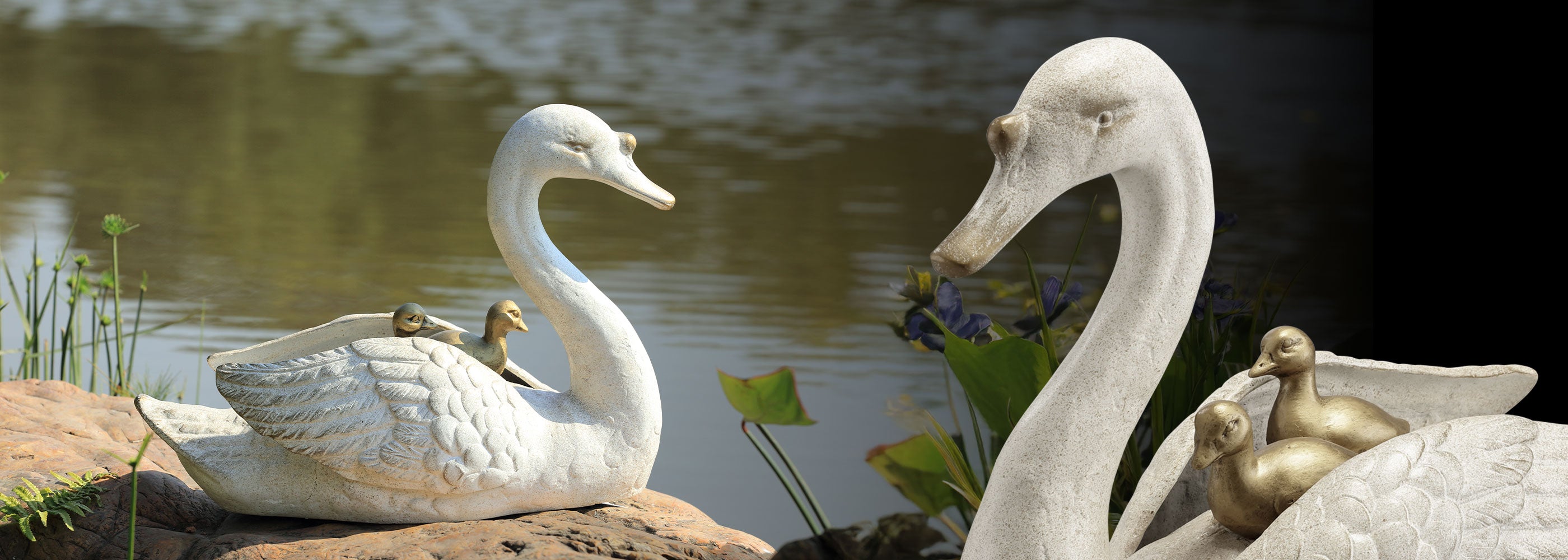 Two white swan statues with a baby swan on a rock by a body of water.