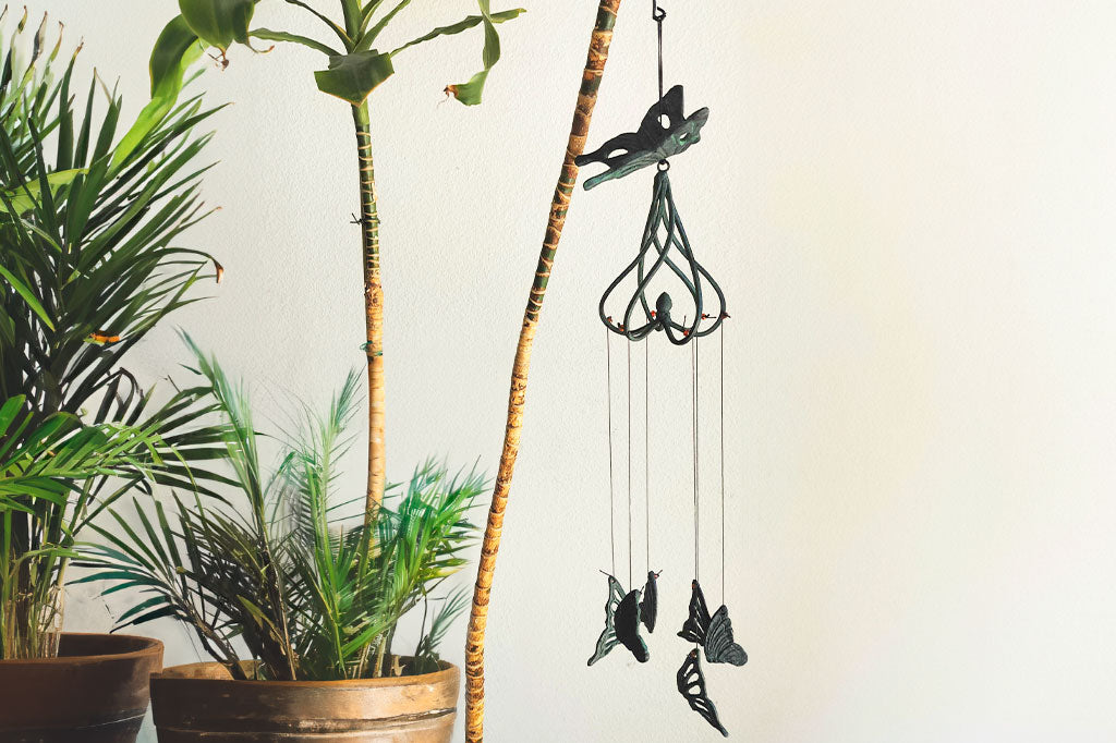 cast metal butterfly and swirl wind art suspended from indoor potted palm branch